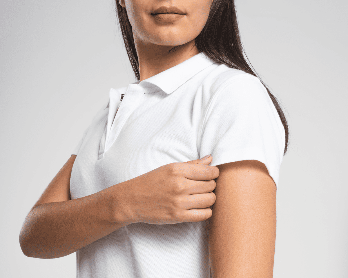 Mujer joven ajustándose la manga de un polo blanco de uniforme corporativo. Frescura y profesionalismo garantizados.
