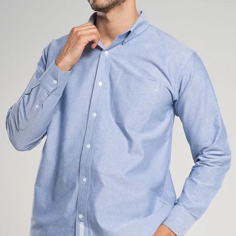 Hombre ajustándose el cuello camisas oxford azul, un gesto que resalta la comodidad y la calidad de la prenda.