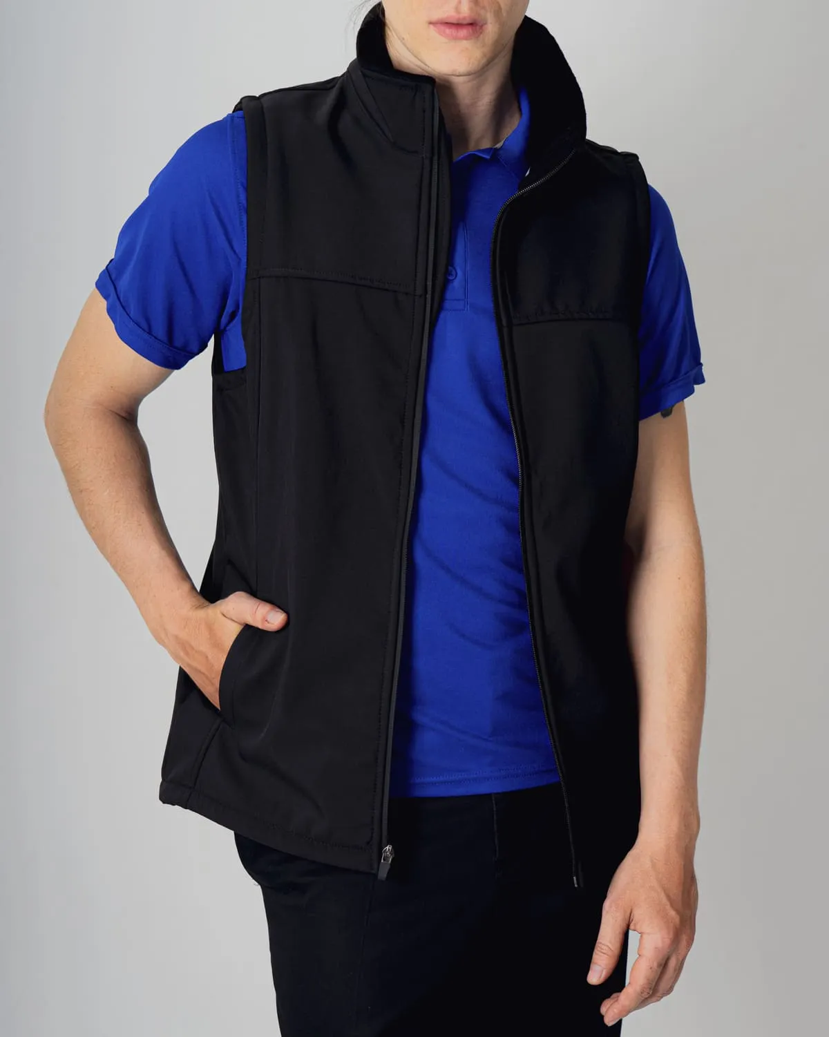 Hombre con chaleco negro y polo azul de uniforme corporativo, con la mano en el bolsillo. Capas versátiles para el trabajo.