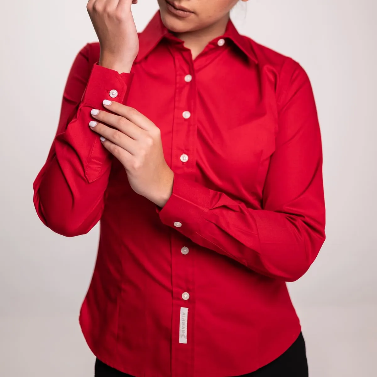 Primer plano de mujer abotonándose el puño de una camisa roja de uniforme corporativo. Atuendo pulcro y profesional.