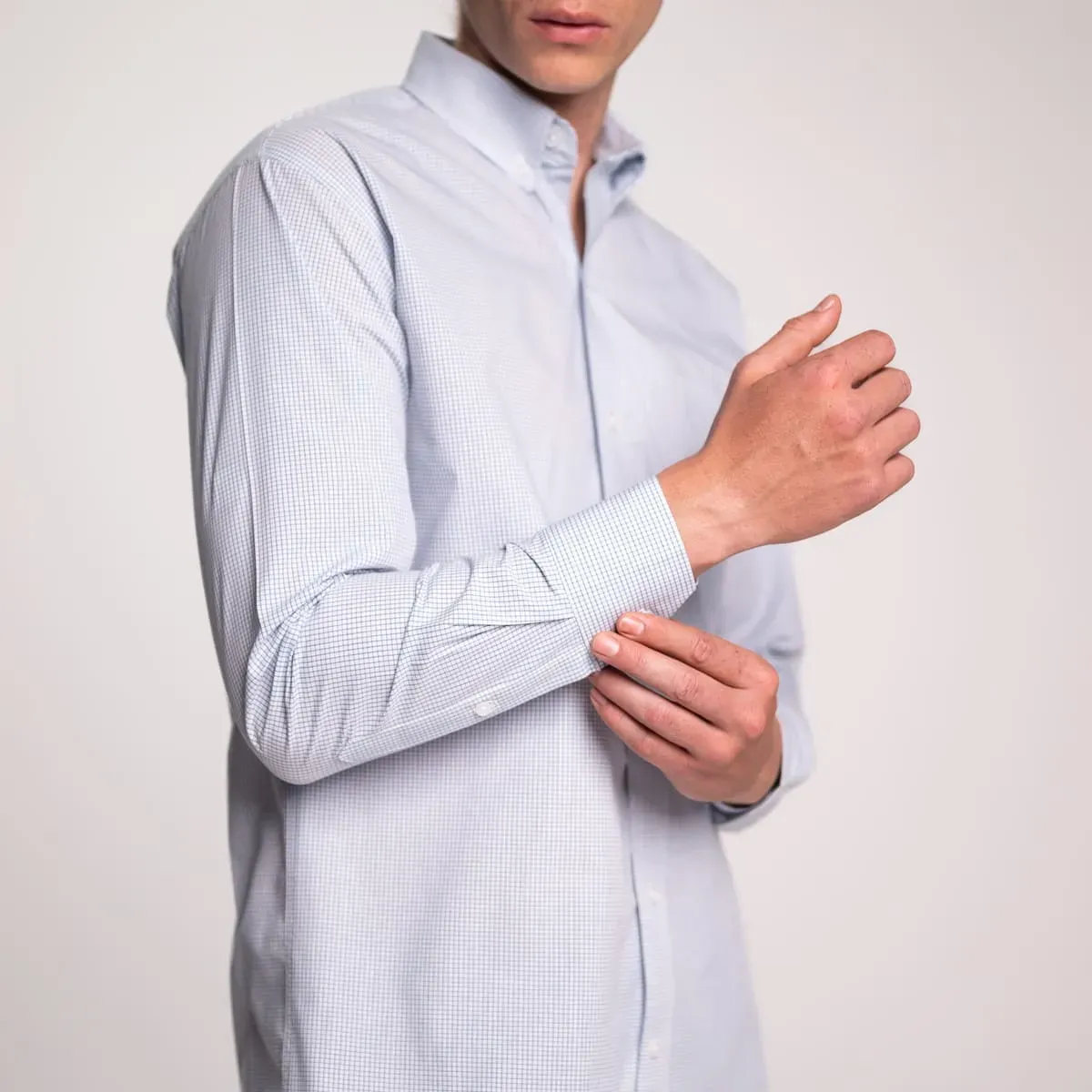 Foto de un joven ajustando la manga de su camisa azul claro de los uniformes corporativos de Airman