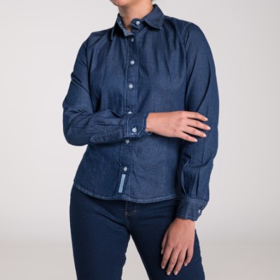 Fotografía de una mujer utilizando una de las camisas de mezclilla de Airman en color azul con botones blancos.