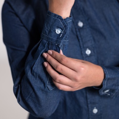 Fotografía de la manga de un modelo de blusas de mezclilla color azul con botones blancos en un fondo claro.
