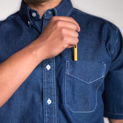 Fotografía de un hombre utilizando una de las camisas de mezclilla de Airman y guardando una pluma en el bolsillo.